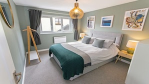 A neatly arranged bedroom with a bed, bedside tables, a hanging light fixture, a radiator, and artwork on the walls. - Oceanside Sleeps 6 Walk to Beach & Stylish (Braunton)