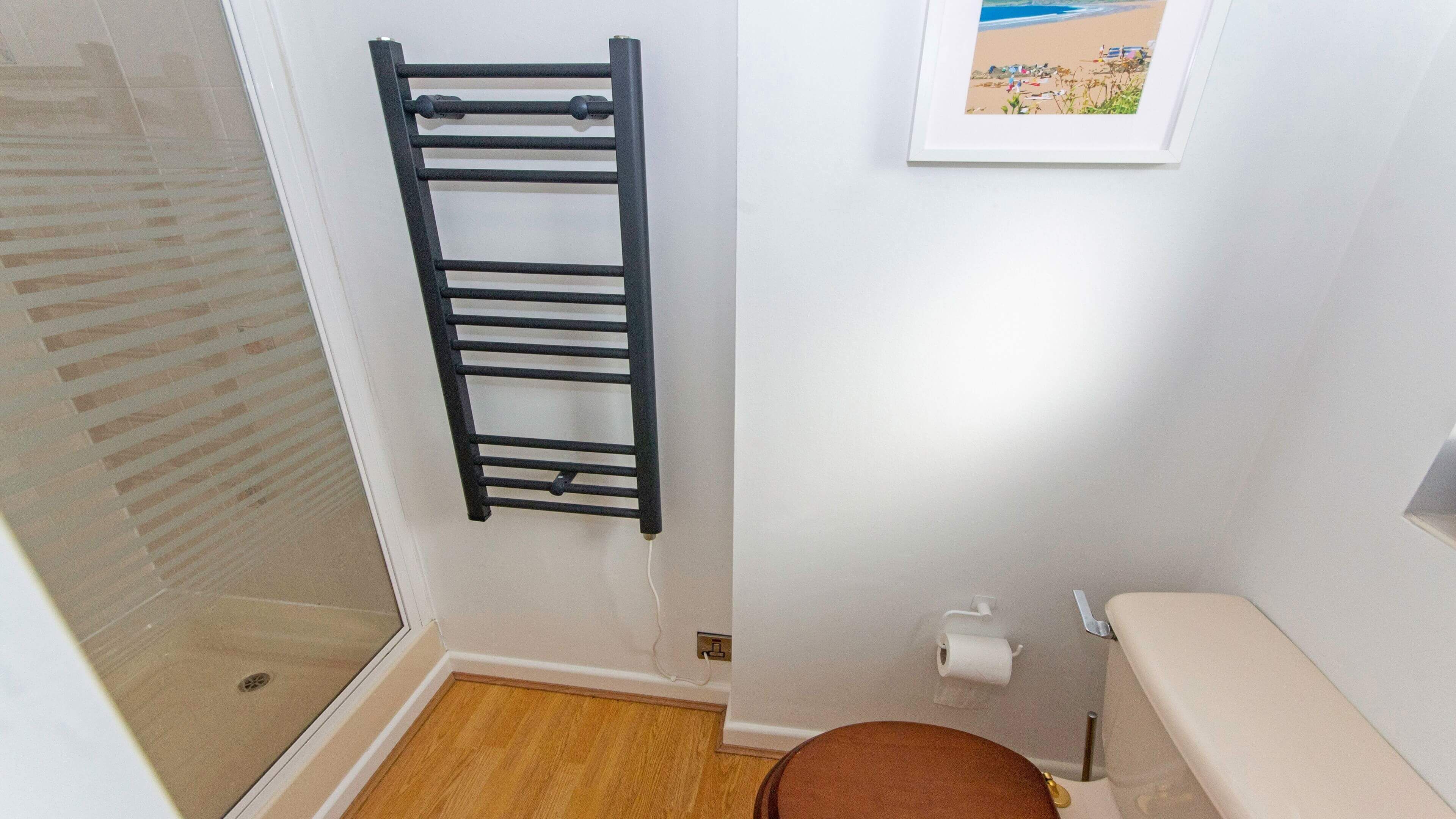 Een badkamer met een zwarte handdoekhouder, een toilet, een inlijsting foto aan de muur, en een houten vloer.