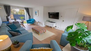 A modern living room with a sofa, armchairs, a TV, and a dining area with a table and chairs. - Oceanside Sleeps 6 Walk to Beach & Stylish (Braunton)