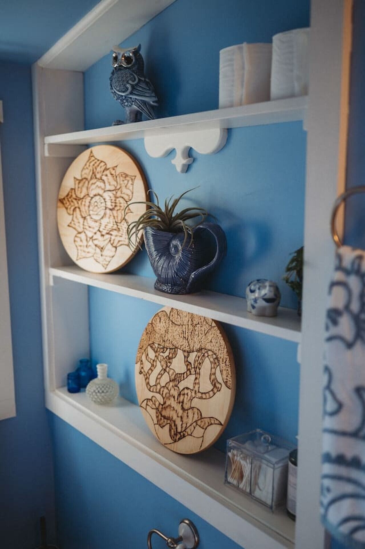 Una estantería con platos decorativos, un búho de cerámica azul y una pequeña planta en maceta.