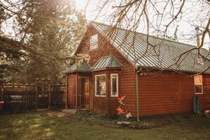 A wooden cabin with a metal roof, surrounded by a wooden fence and a grassy yard.