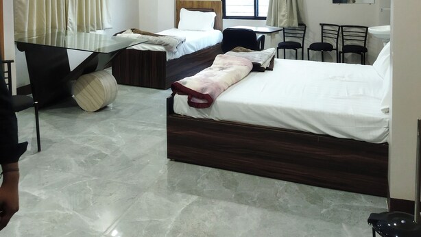 A hotel room with two beds, a desk, chairs, a ceiling fan, and a window with curtains. - SR HOTEL KILERAMA ASHTA  (Ashta)