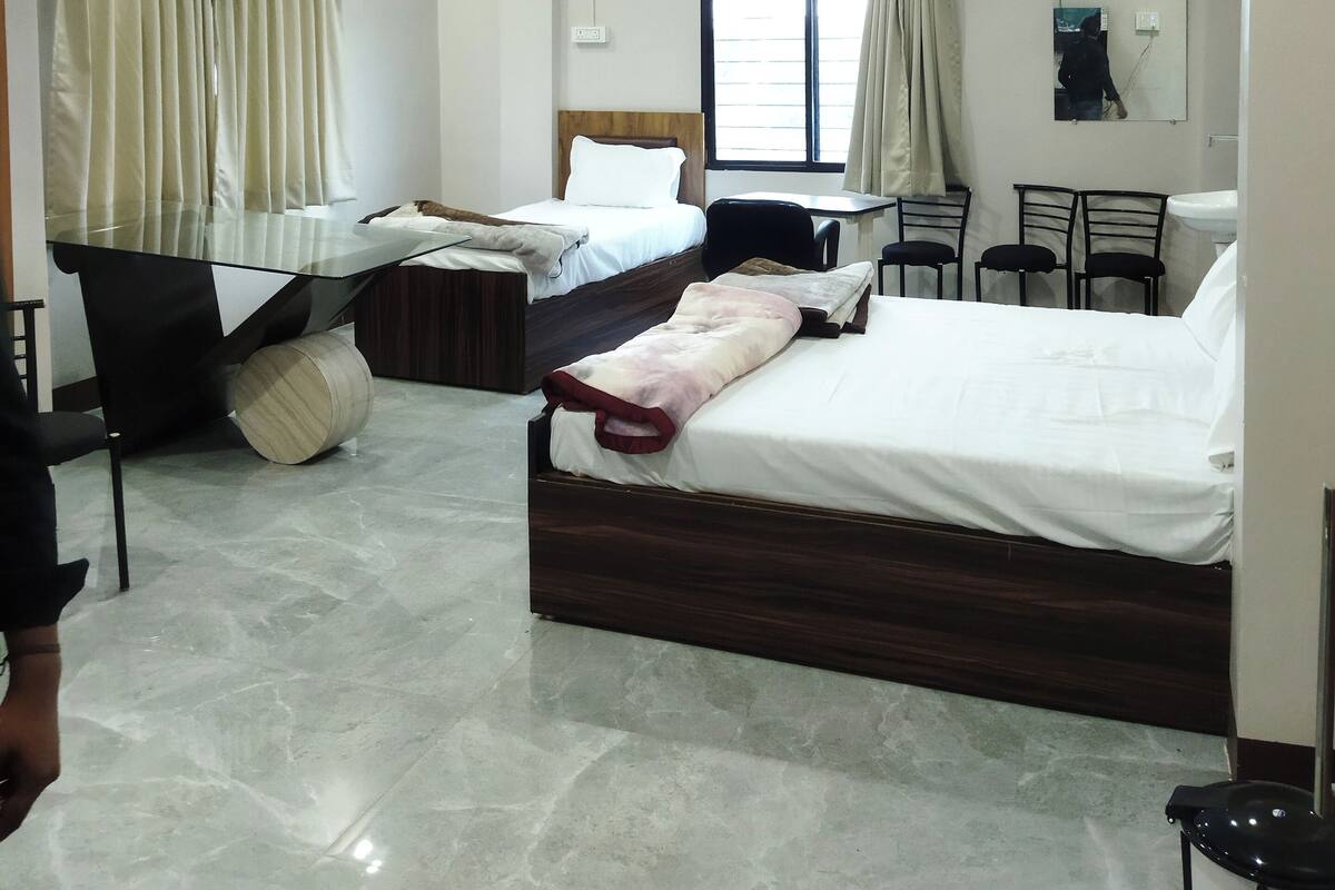 Une chambre d’hôtel avec deux lits, un bureau, des chaises, un ventilateur de plafond et une fenêtre avec des rideaux.