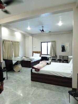 Une chambre d’hôtel avec deux lits, un bureau, des chaises, un ventilateur de plafond et une fenêtre avec des rideaux.