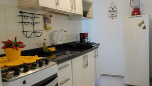 A kitchen with white cabinets, a stove, a sink, and a refrigerator. There is a yellow rug on the floor and a plant on the counter.