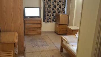 Una habitación pequeña con cama, escritorio, cómoda y televisor.