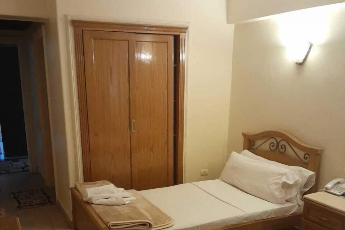 Ein Hotelzimmer mit einem hölzernen Bett, einem Holzschrank, einem Nachttisch mit Lampe und einem kleinen Schreibtisch mit Telefon.