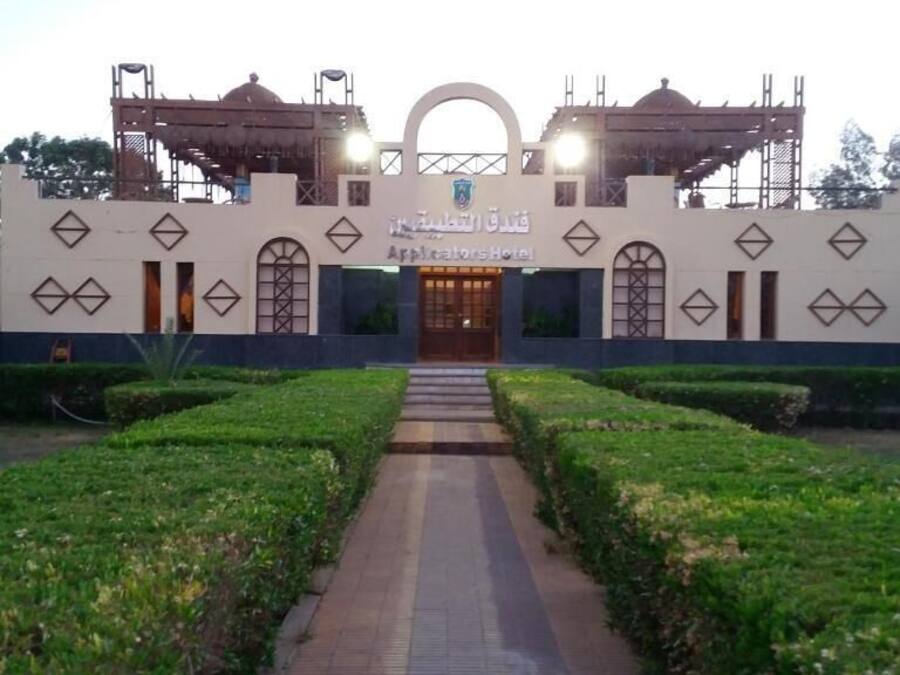 The exterior of the Applicators Hotel with a symmetrical facade, a central entrance, and a well-maintained garden with a pathway leading to the entrance.