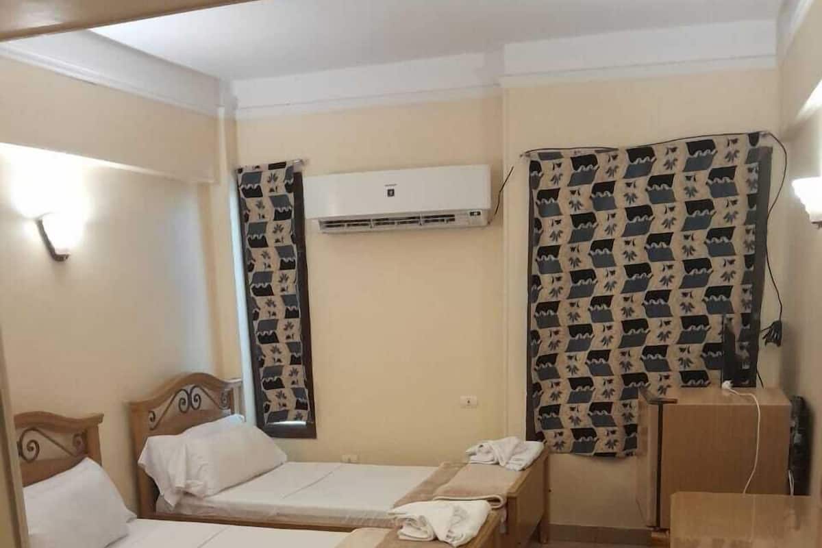 Ein Hotelzimmer mit drei hölzernen Betten, beigen Wänden und gemusterten Vorhängen.