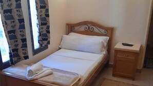 Un lit bien fait, avec du linge de lit blanc, une tête de lit en bois et une table de chevet sur laquelle se trouve une télécommande.