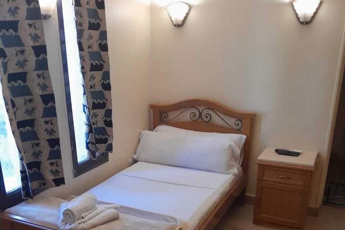 Ein ordentlich bezogenes Bett mit weißer Bettwäsche, einem hölzernen Kopfteil und einem Nachttisch mit Fernbedienung.