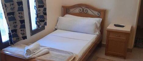 A neatly made bed with white linens, a wooden headboard, and a bedside table with a remote control.
