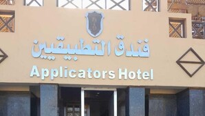 L’entrée de l’hôtel Applicators est signalée par une enseigne en arabe et en anglais. Un escalier mène à l’entrée, et l’architecture moderne présente des motifs géométriques.