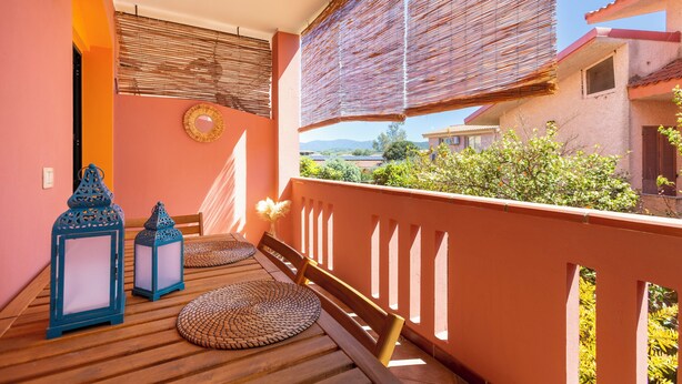Un balcon doté d’un plancher en bois, de deux lanternes bleues, d’un tapis tressé et d’une chaise en bois.