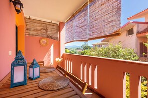 Un balcon doté d’un plancher en bois, de deux lanternes bleues, d’un tapis tressé et d’une chaise en bois.