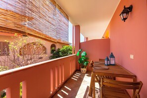 A balcony with a wooden table and chairs, a potted plant, and a wall-mounted lantern.