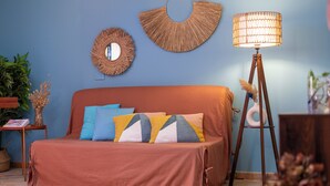 Un lit avec une couvre-lit marron et plusieurs oreillers, un miroir rond, une décoration murale tissée et une lampe sur pied.