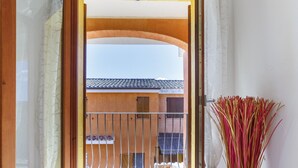 Een hotelkamer met een bed, een raam met gordijnen, uitzicht op een buitenbalkon en een bloemenvaas.