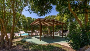 A covered outdoor area with a table and chairs, surrounded by trees and a barbecue grill. - Countryside house - 6 (Carbonia)