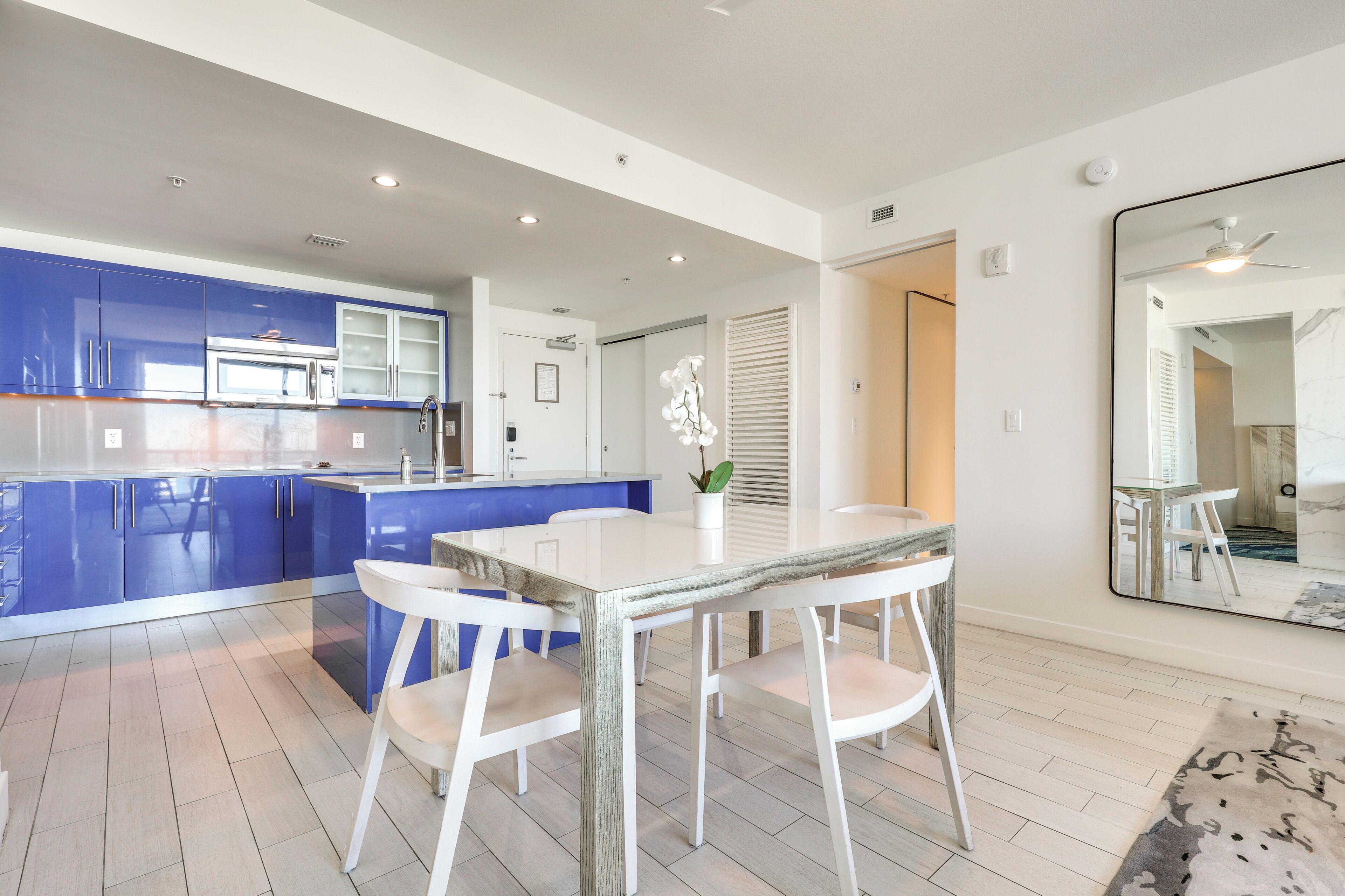 A modern kitchen with blue cabinets, a white dining table, and a large mirror.