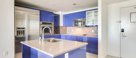A modern kitchen with blue cabinets, stainless steel appliances, and a large island.