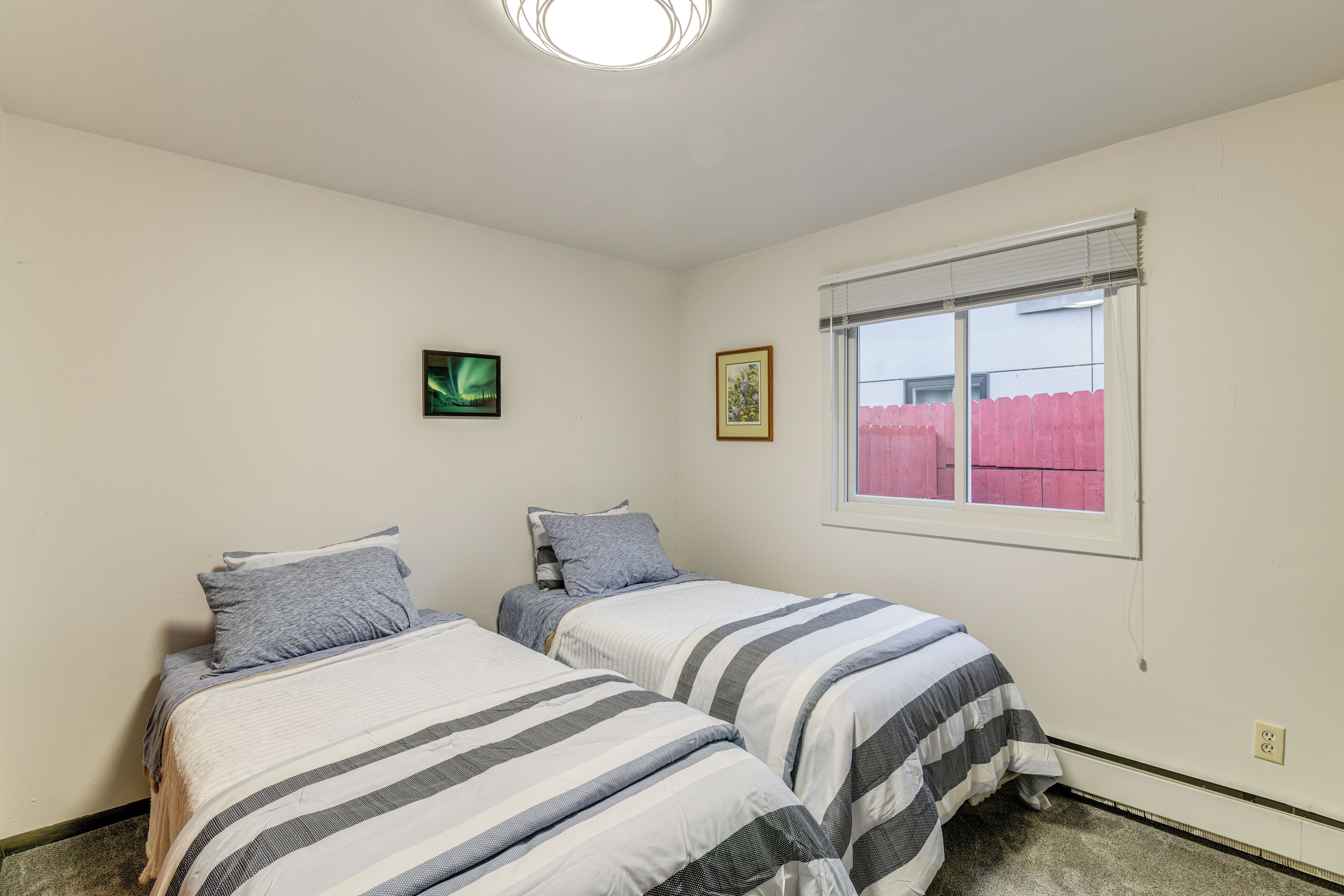 Un dormitorio con dos camas, una ventana con persianas y una lámpara fijada a la pared.