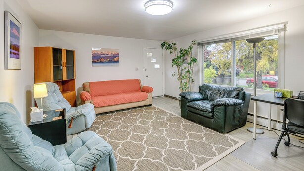 Ein Wohnzimmer mit einer Couch, einem Sessel, einem Schreibtisch und einem großen Fenster.