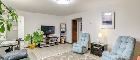 Una sala de estar con televisor, dos sillones, un sofá, una mesa de centro y una planta.