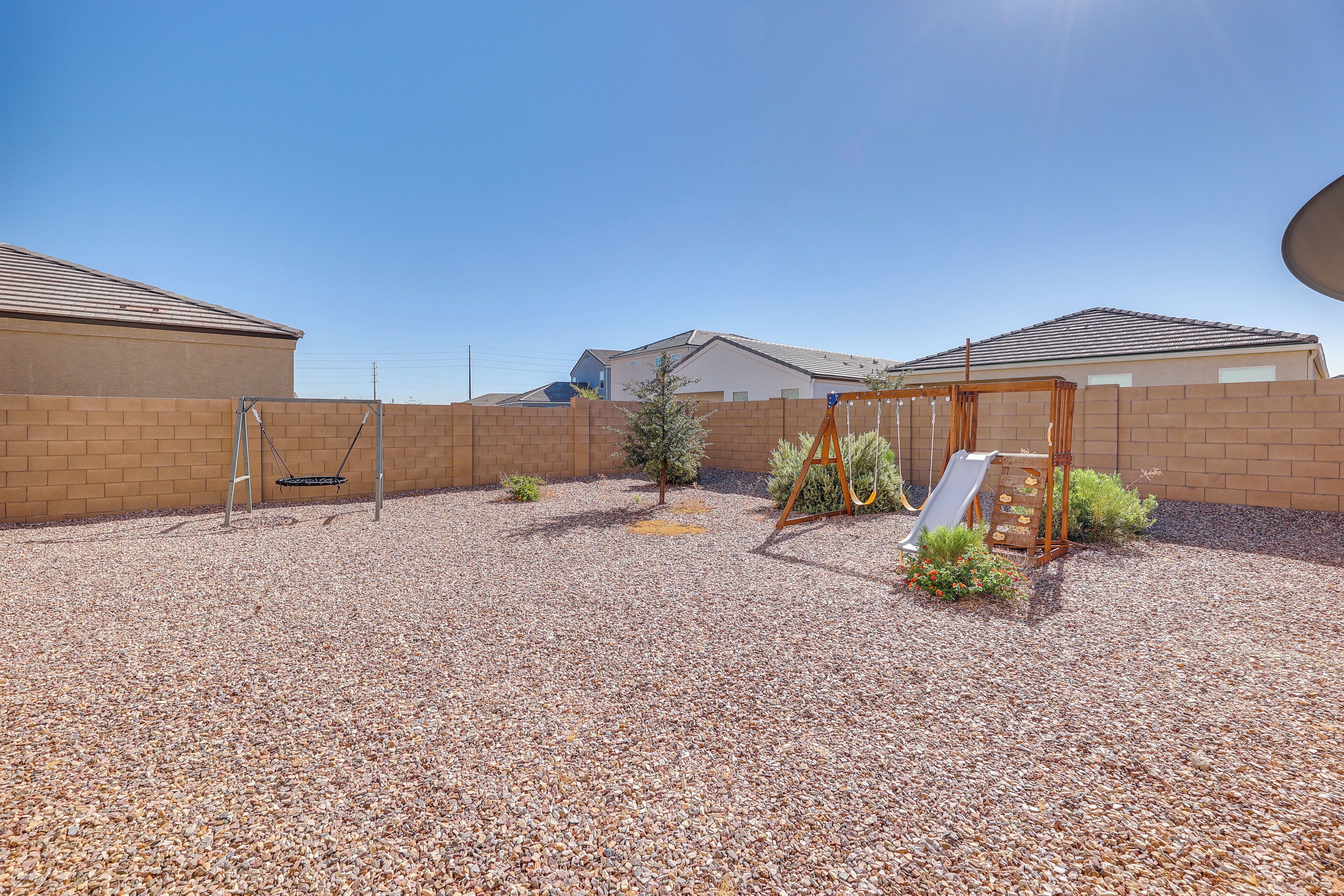 A backyard with a swing set, a small tree, and a brick wall.