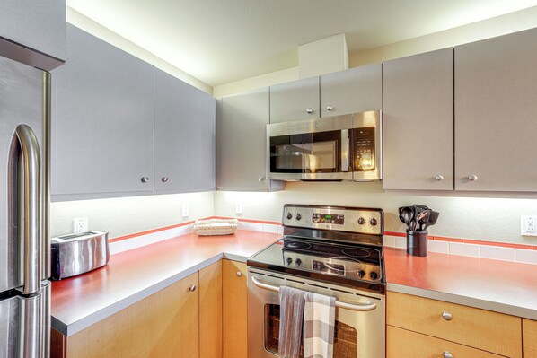 Una cocina moderna con electrodomésticos de acero inoxidable, armarios de madera y encimera roja.