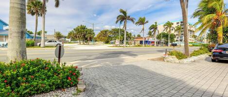 A paved sidewalk with palm trees and a street.