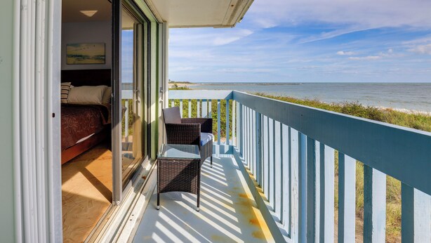 A balcony with a bed and chairs, overlooking a beach and ocean. - Oceanside: Beachfront Fort Pierce Retreat (Fort Pierce)