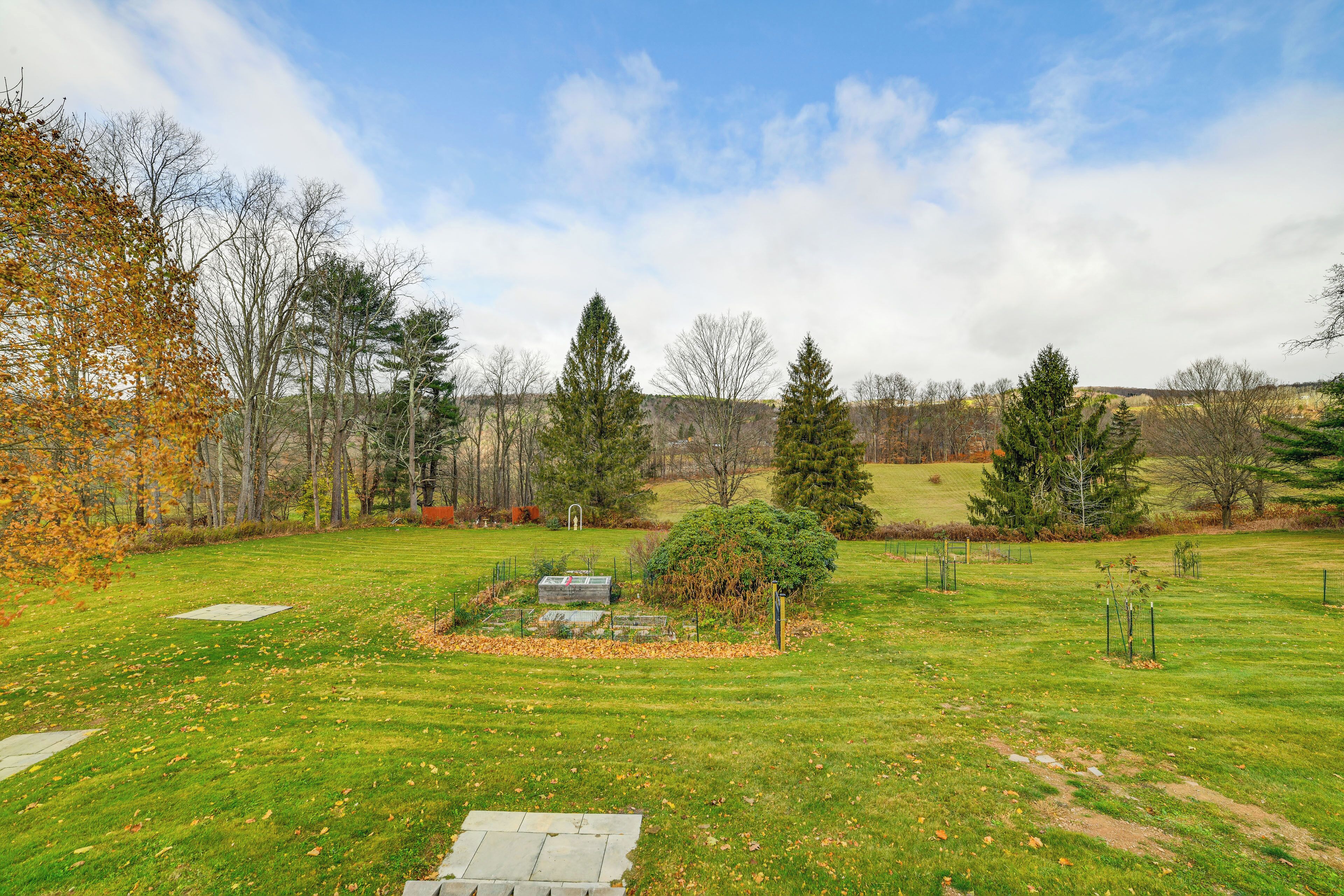 A grassy field with a stone pathway, trees, and a clear sky.