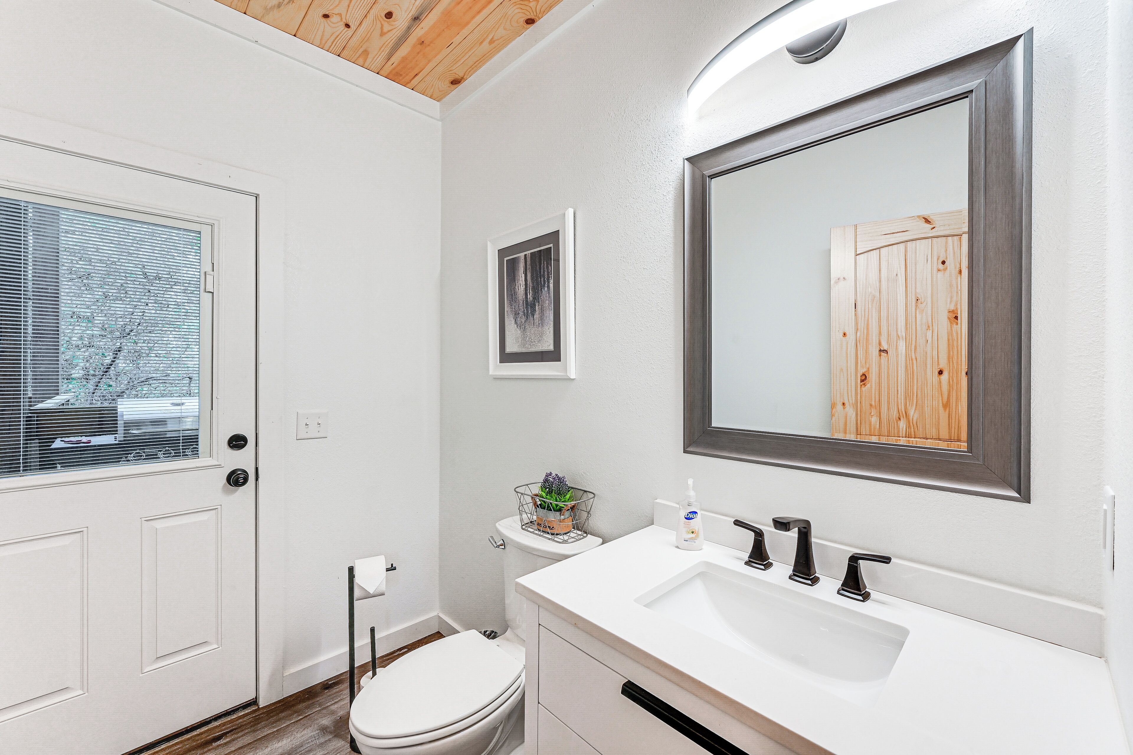Une salle de bain moderne avec un lavabo blanc, des robinets noirs, un plafond en bois et un miroir encadré.