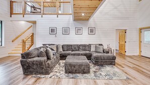 Ein geräumiges Wohnzimmer mit einer großen Eckcouch, einer Holzbalkendecke und einer Treppe, die zu einer oberen Ebene führt.