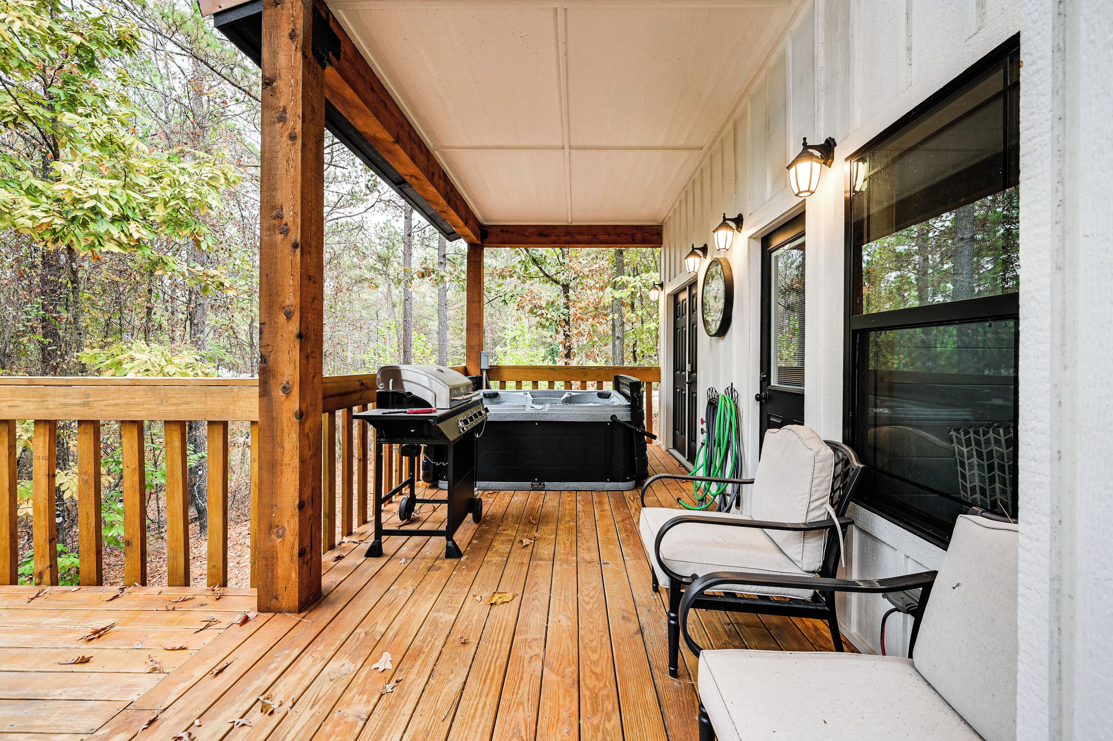 A covered deck with a grill, chairs, and a view of the forest.