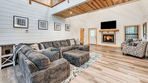 Ein geräumiges Wohnzimmer mit einer großen Eckcouch, einem gemusterten Sessel und einem Kamin.