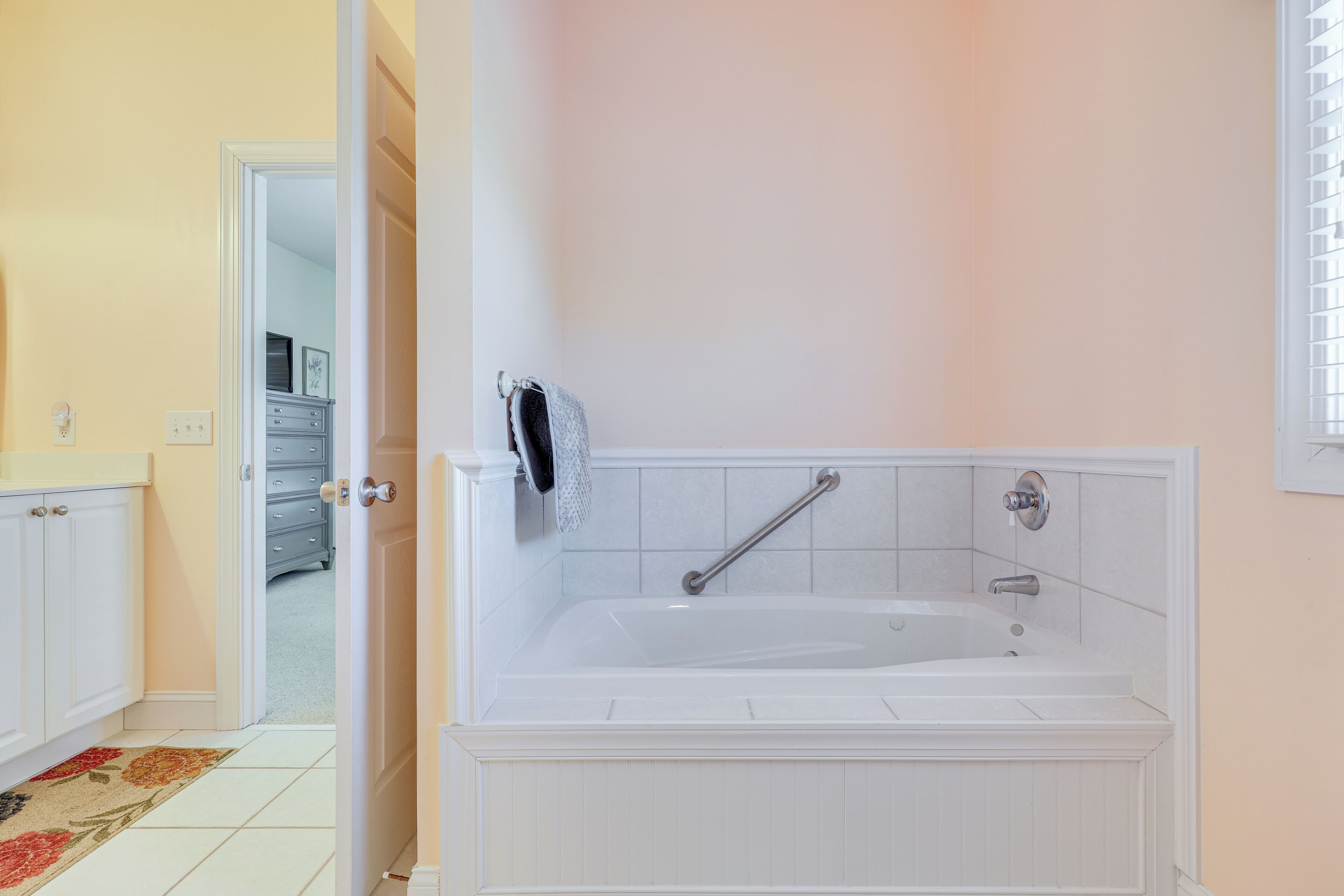 A bathroom with a white bathtub, a towel rack, and a door leading to another room.