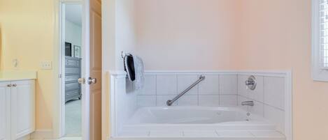 A bathroom with a white bathtub, a towel rack, and a door leading to another room.