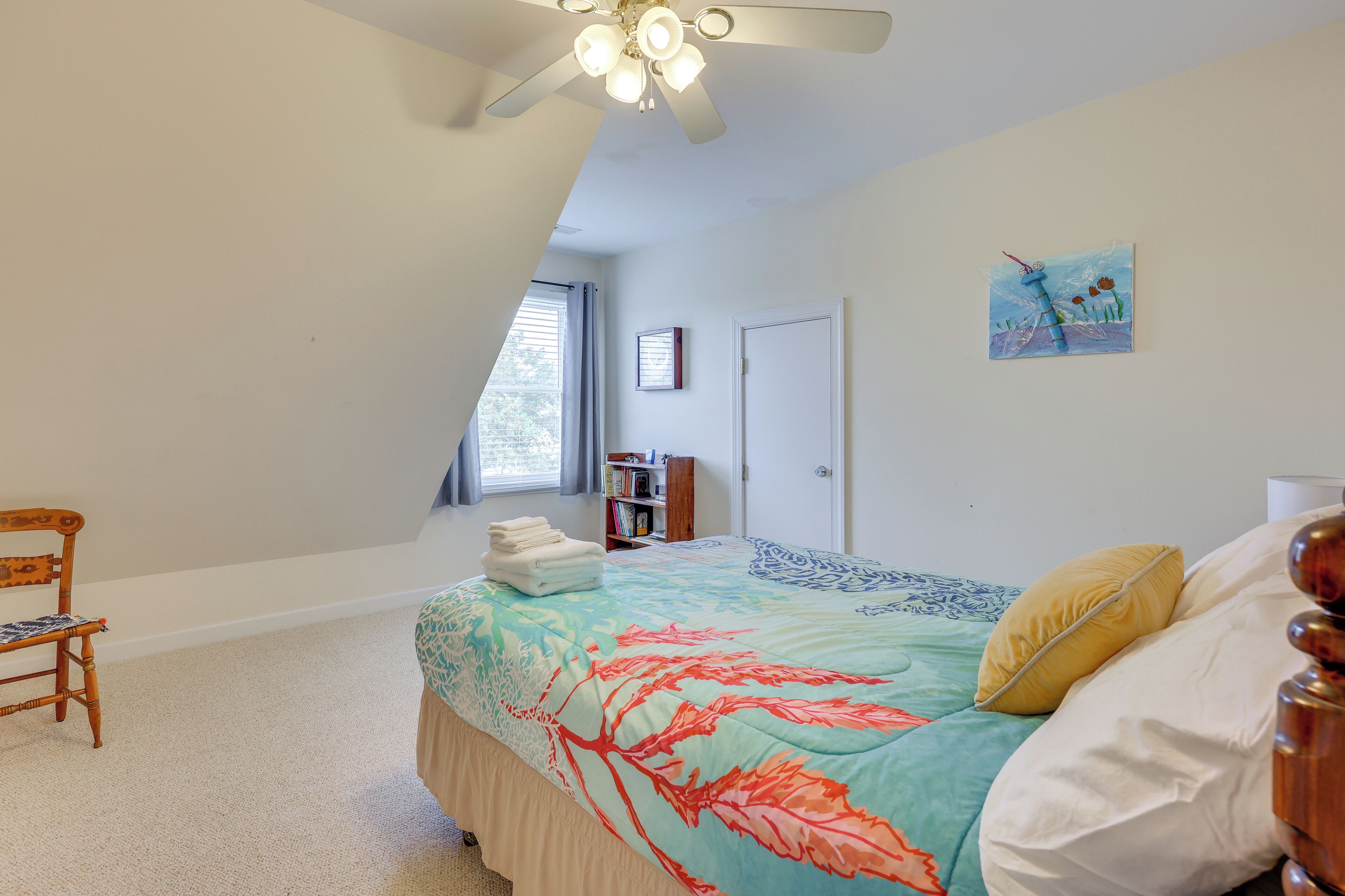 A bedroom with a bed, a chair, a ceiling fan, a bookshelf, and a door.