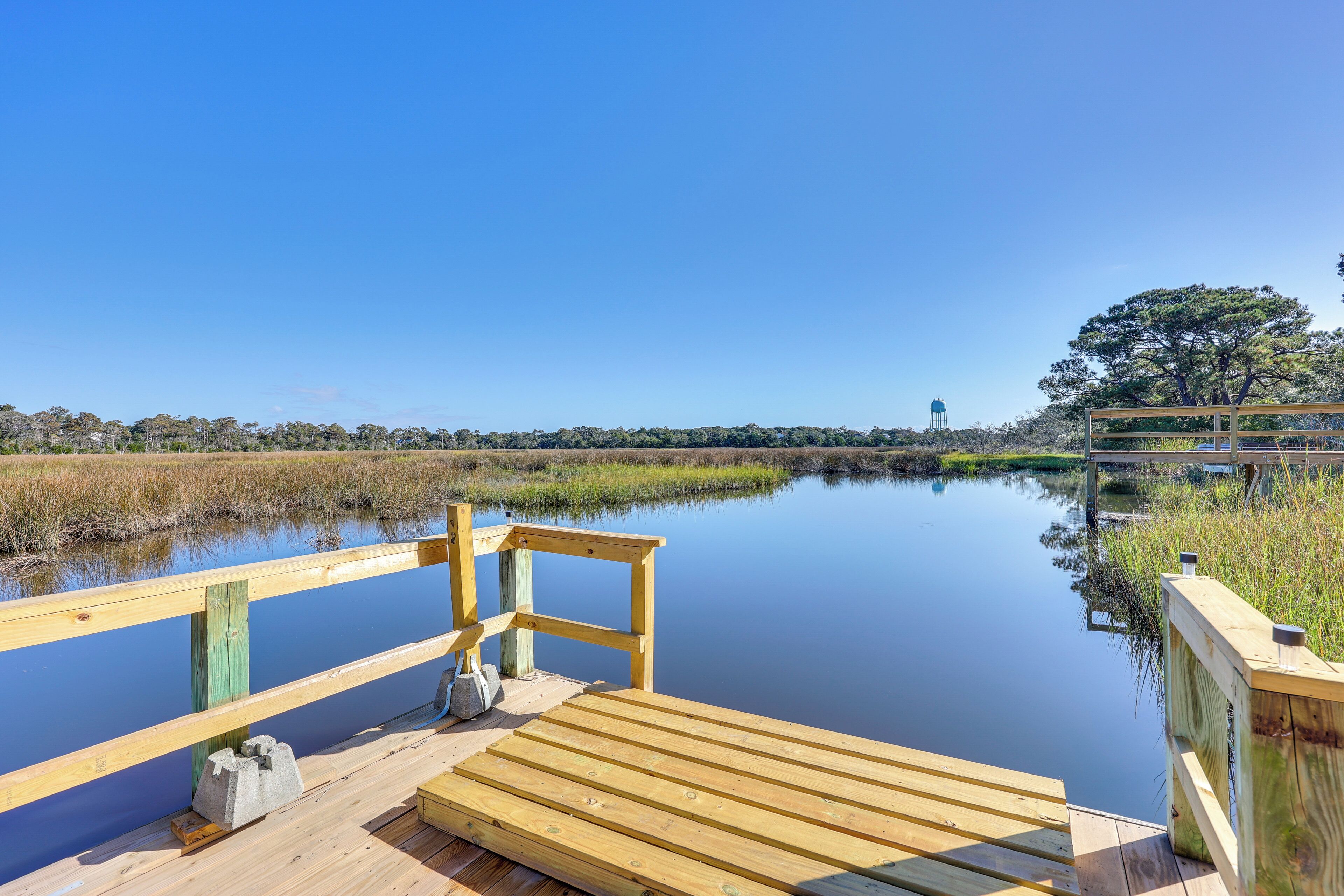 A wooden dock extending into calm water with a clear sky and distant trees.