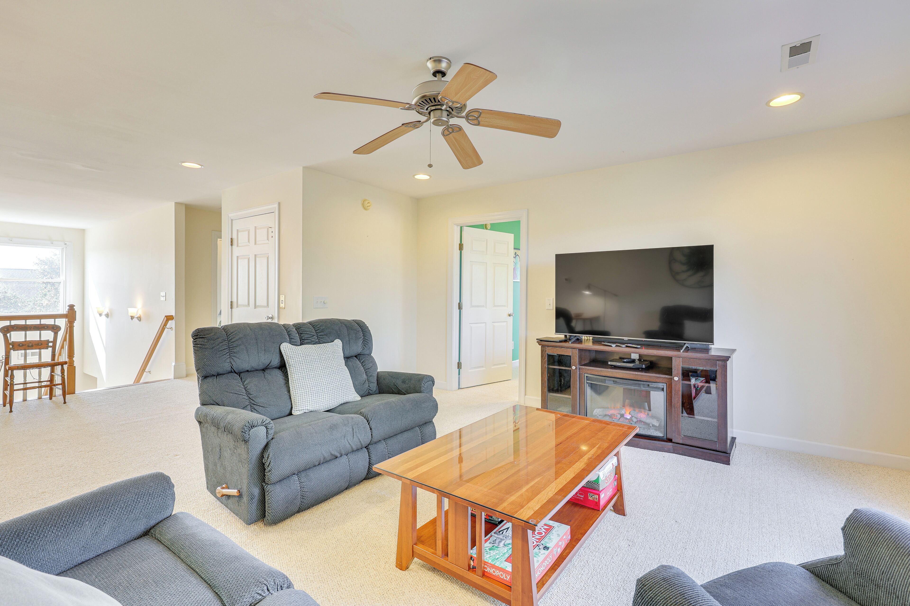 A living room with a grey sofa, a wooden coffee table, a ceiling fan, and a TV on a wooden cabinet.