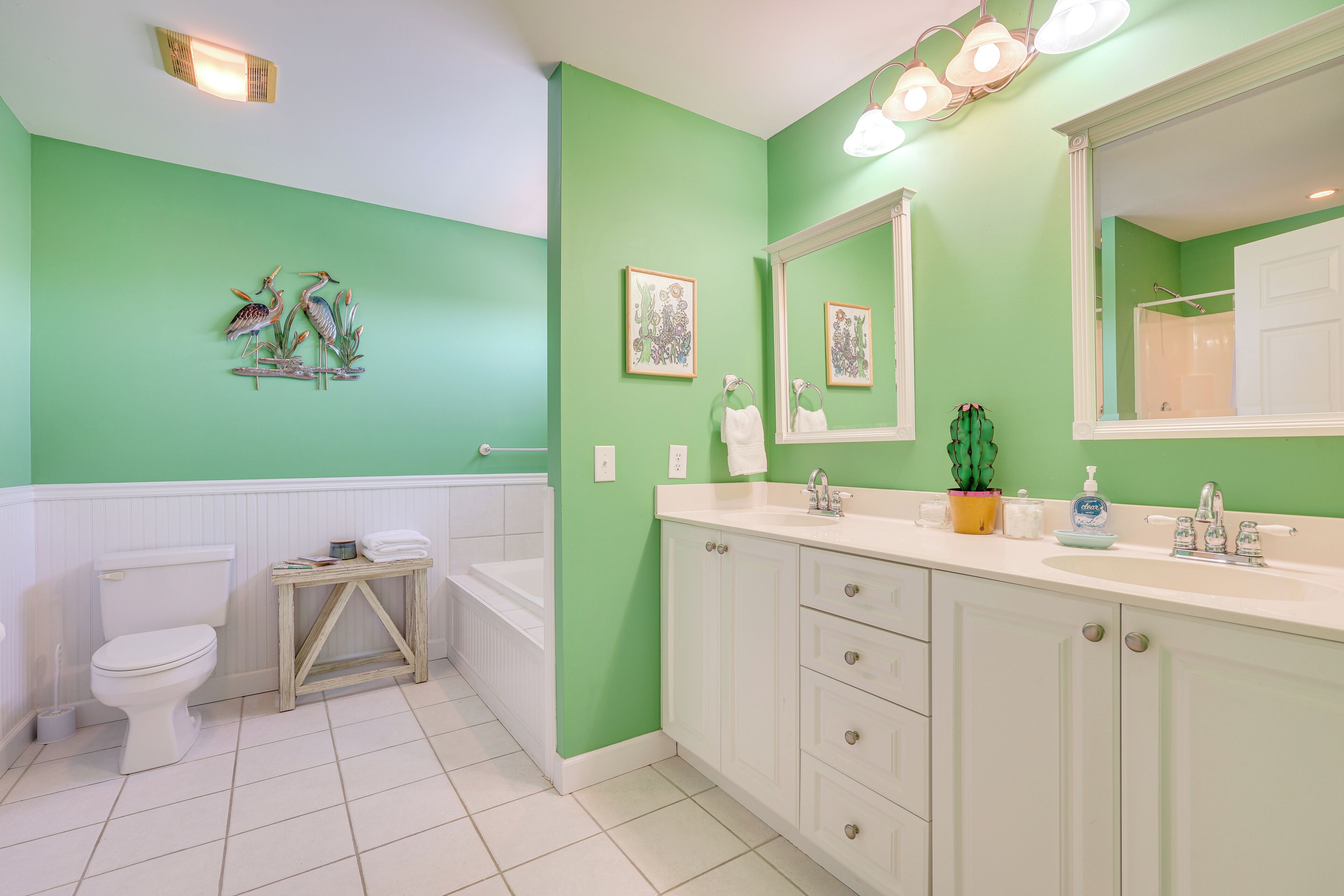 Un baño con paredes verdes, accesorios blancos y un espejo grande.