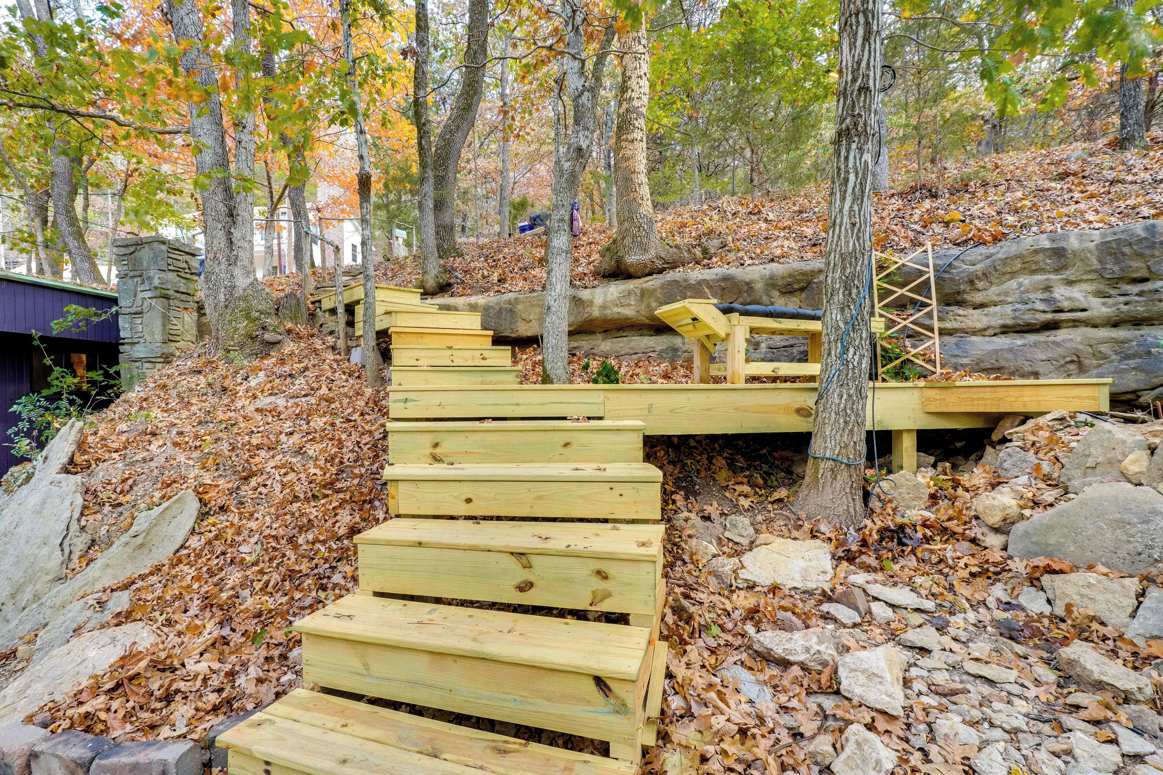 A wooden staircase leading up a rocky slope in a forested area with autumn leaves.