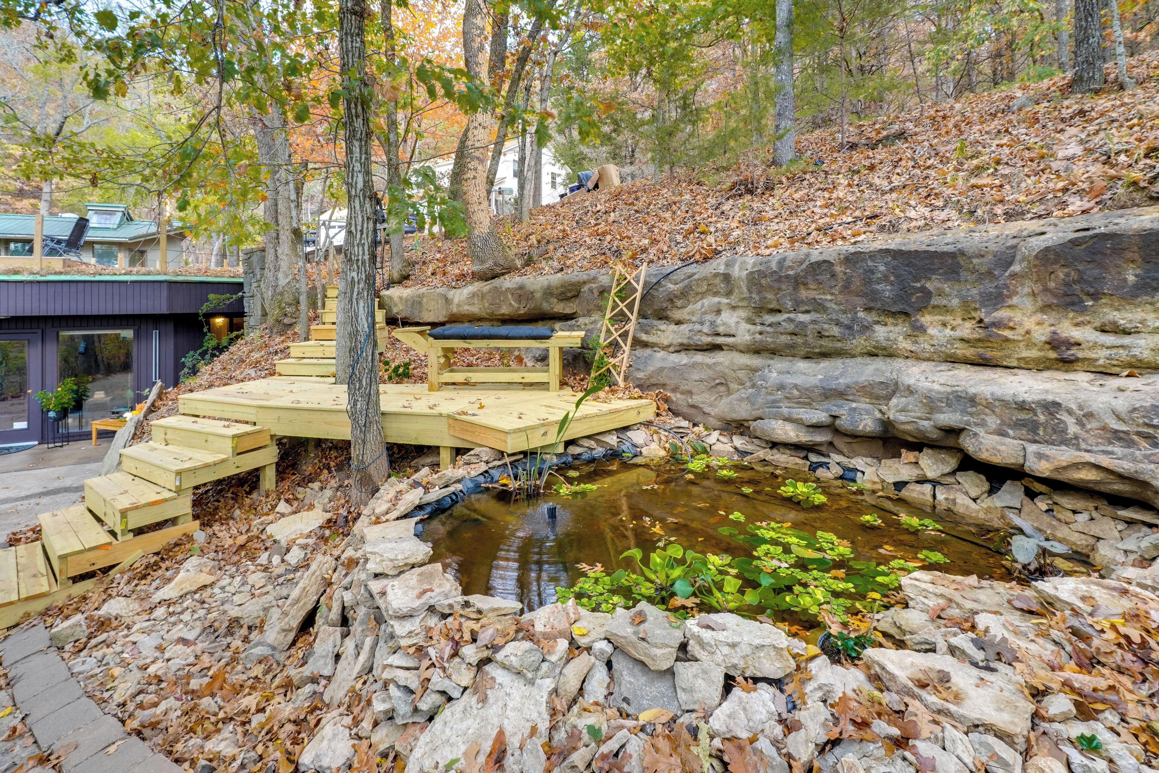 A stone retaining wall, a wooden deck, and a small pond with plants.