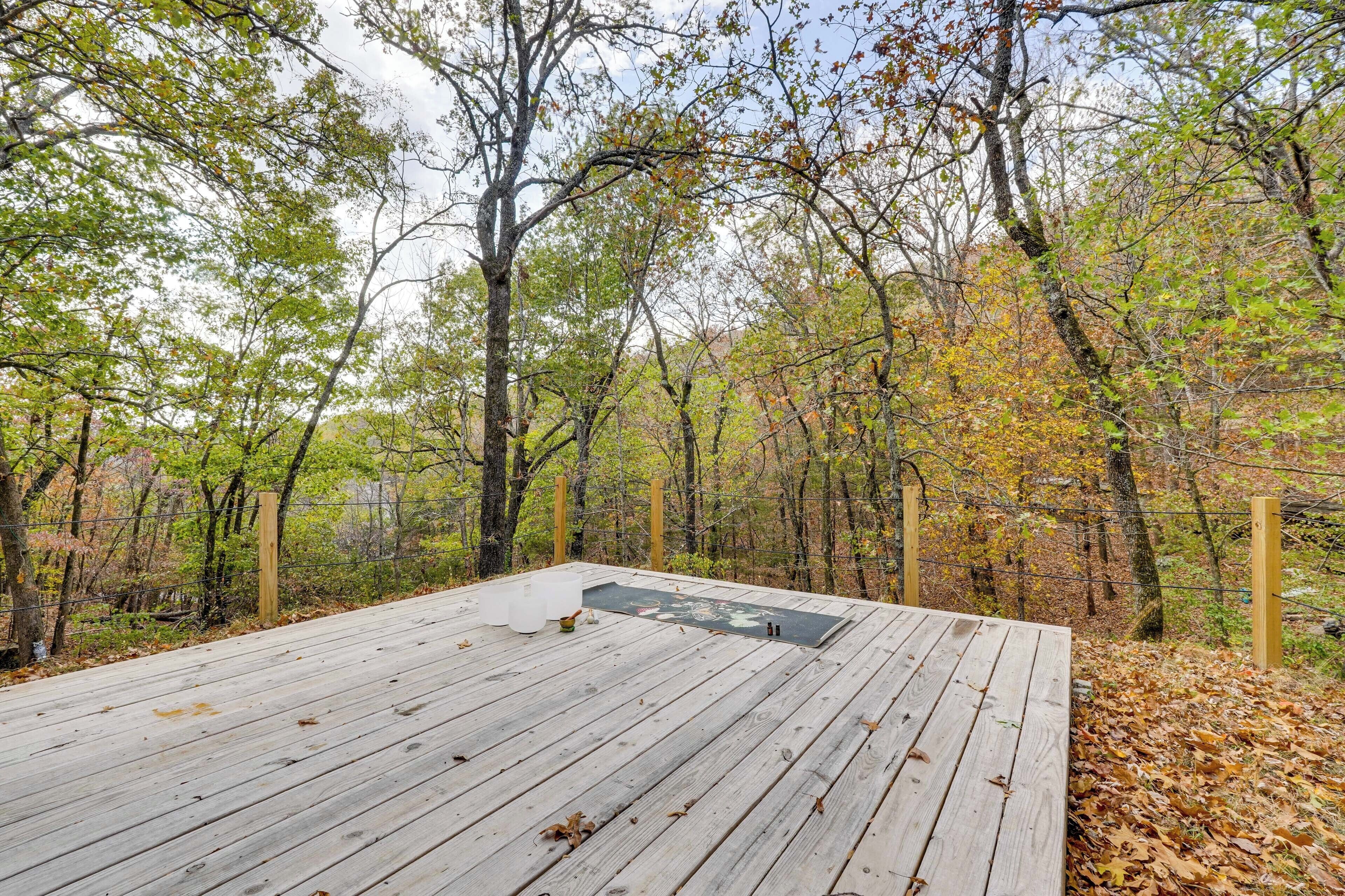 A wooden deck with a metal grate, surrounded by trees with autumn foliage.