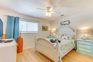 Une chambre à coucher comprenant un lit, des tables de chevet, un ventilateur de plafond, une fenêtre avec des rideaux et un luminaire fixé au mur.