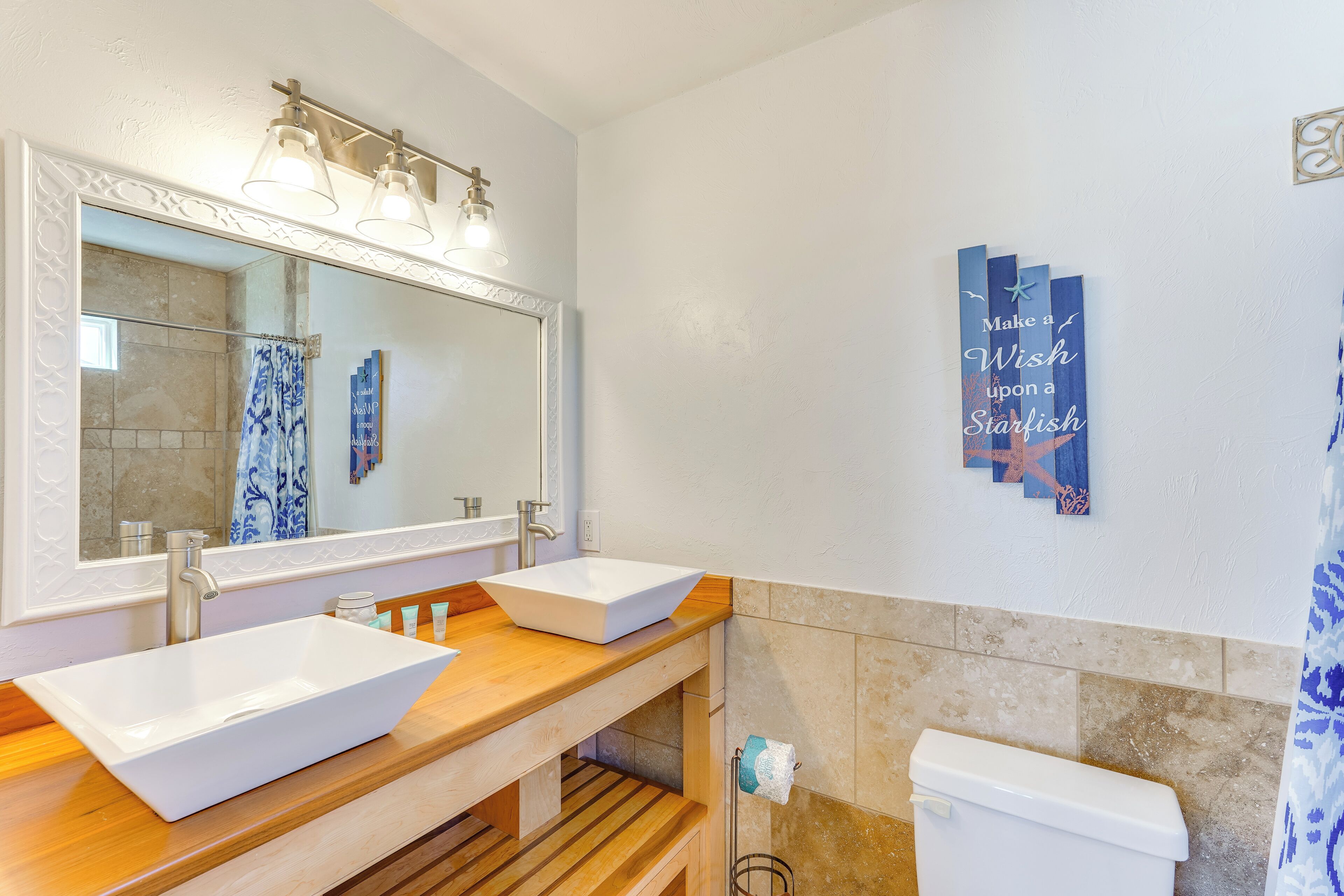 A bathroom with a white sink, a mirror, and a toilet. There is a towel rack and a wall decoration with text.
