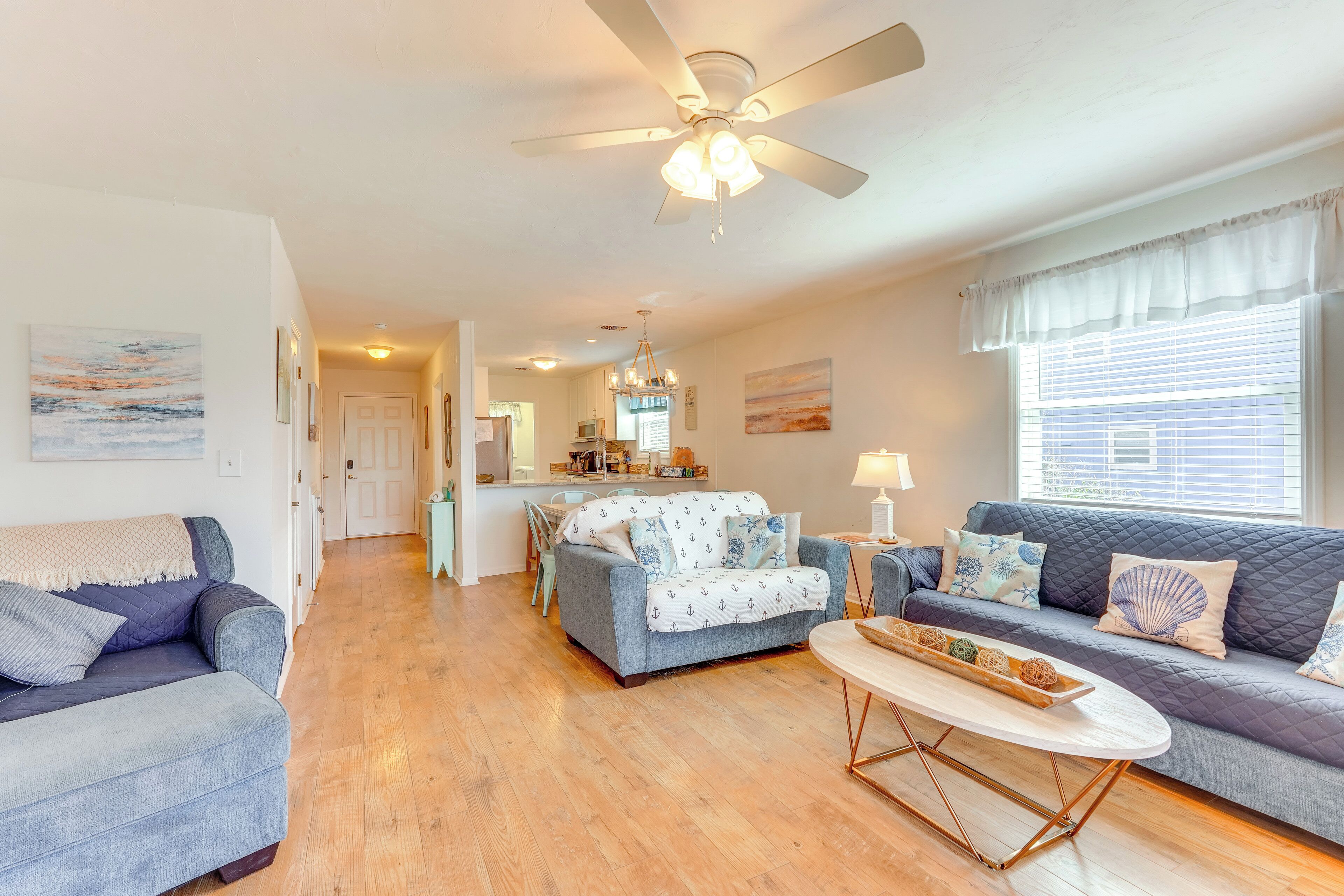 A spacious living room with a ceiling fan, a dining area with a chandelier, and a kitchen in the background.
