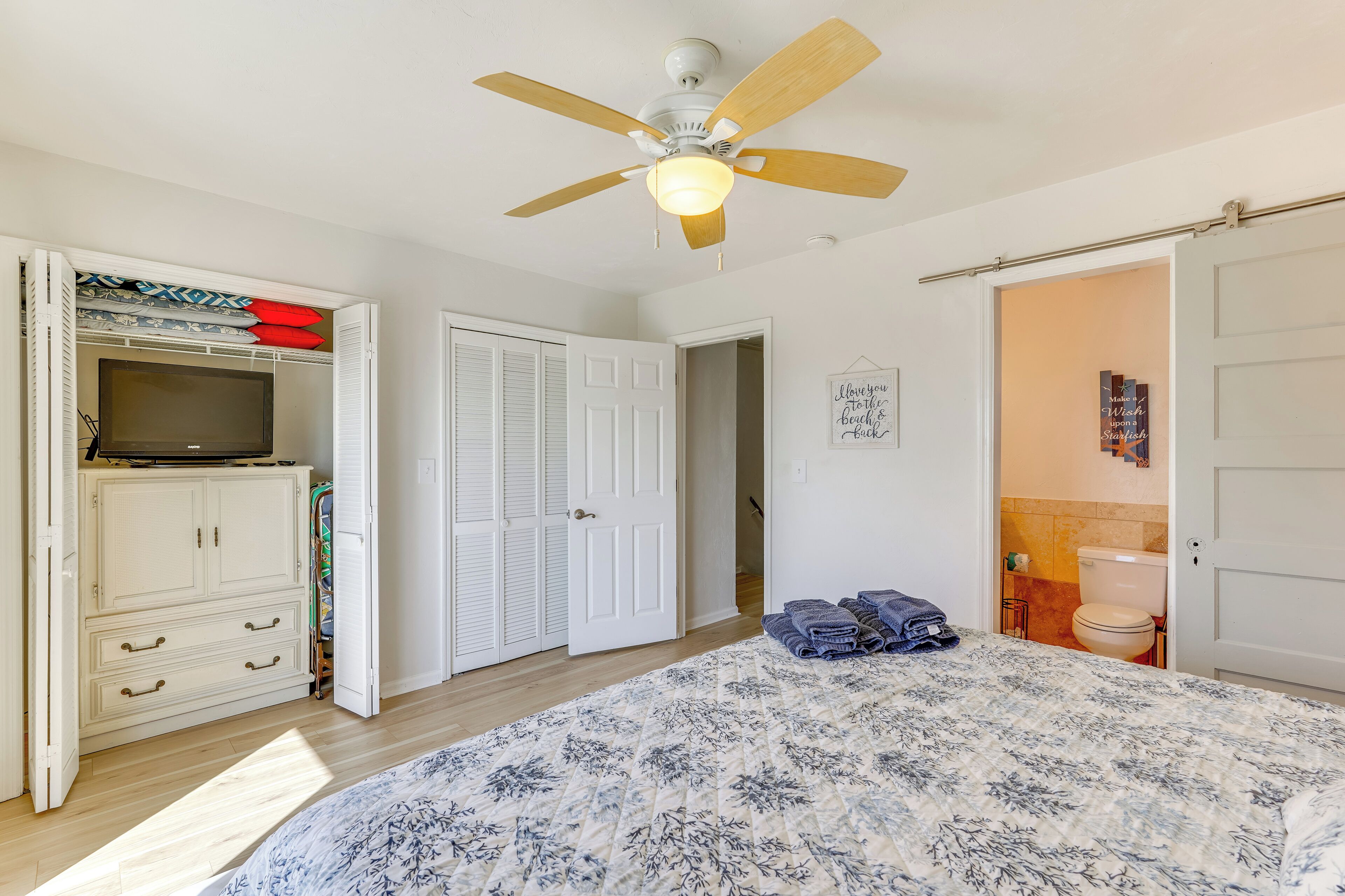 A bedroom with a bed, a wardrobe, a ceiling fan, a door, and a bathroom visible through an open door.